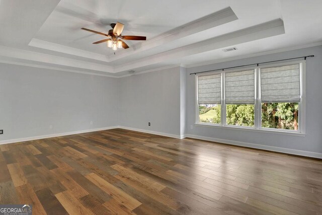 empty room with ceiling fan, a raised ceiling, ornamental molding, and dark wood-type flooring