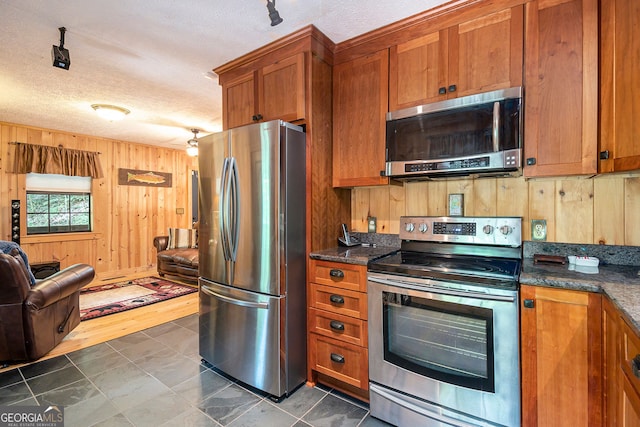 kitchen featuring dark stone countertops, a textured ceiling, wood walls, dark hardwood / wood-style flooring, and appliances with stainless steel finishes