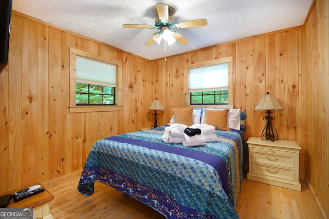 bedroom with a ceiling fan, wooden walls, wood finished floors, and a textured ceiling
