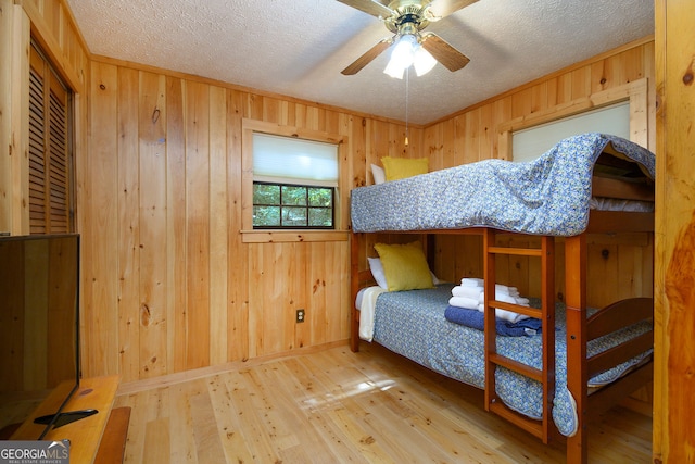 bedroom featuring hardwood / wood-style floors, ceiling fan, wooden walls, and a textured ceiling