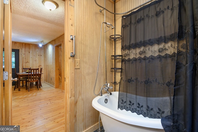 bathroom with a textured ceiling, wood-type flooring, wooden walls, and shower with separate bathtub