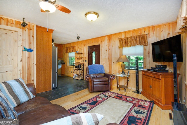 living room featuring wood walls, ceiling fan, dark hardwood / wood-style floors, and a textured ceiling