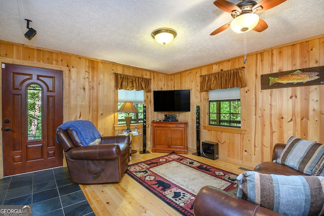 tiled living room with ceiling fan, wooden walls, and a textured ceiling