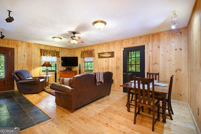 living room with a textured ceiling, ceiling fan, wood walls, and wood-type flooring