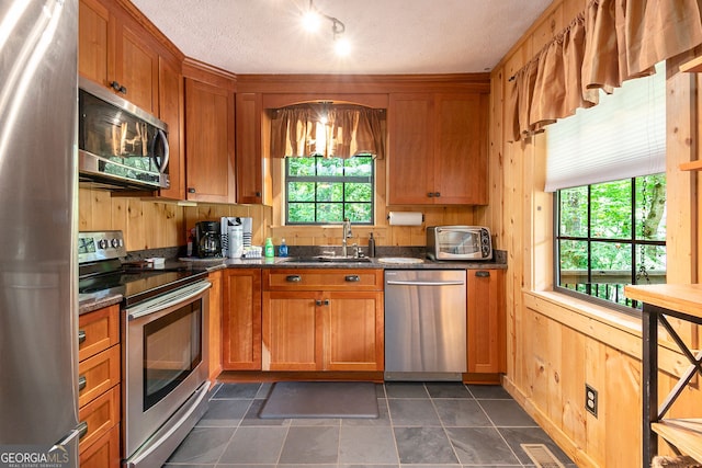 kitchen featuring a sink, wooden walls, visible vents, appliances with stainless steel finishes, and brown cabinetry