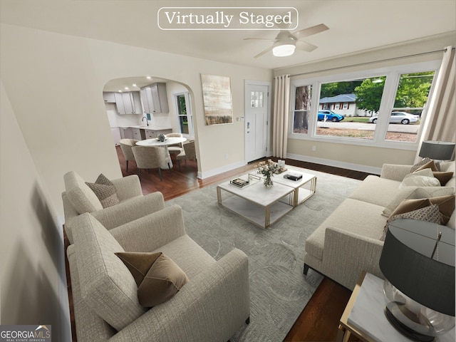 living room featuring arched walkways, a ceiling fan, baseboards, and wood finished floors