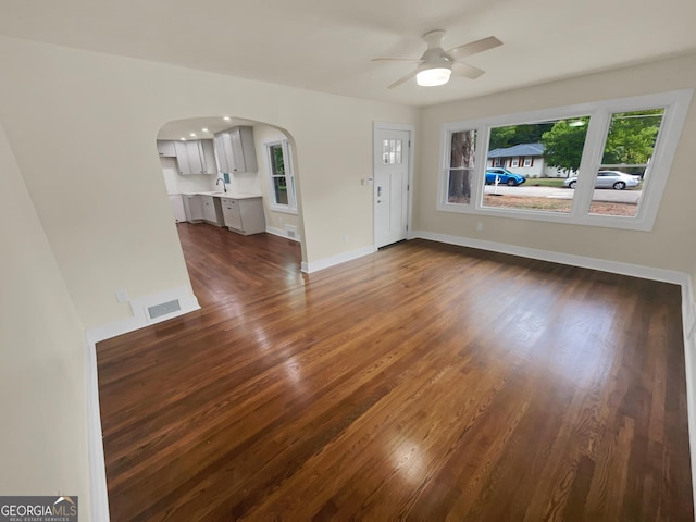 unfurnished living room with visible vents, dark wood-type flooring, baseboards, arched walkways, and a ceiling fan