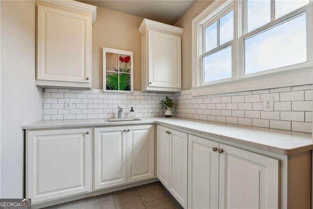 kitchen featuring light stone countertops, backsplash, sink, light tile patterned floors, and white cabinets