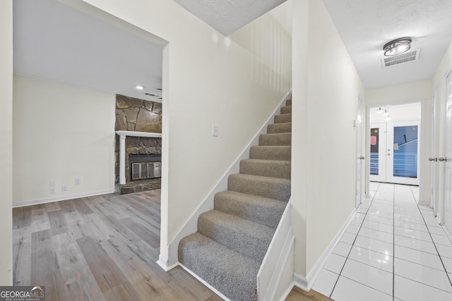 staircase featuring a textured ceiling, hardwood / wood-style flooring, and a stone fireplace