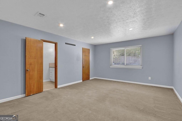 unfurnished bedroom featuring visible vents, baseboards, ensuite bathroom, a textured ceiling, and carpet floors