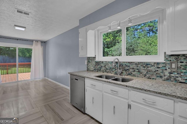 kitchen featuring a wealth of natural light, stainless steel dishwasher, light stone counters, and sink