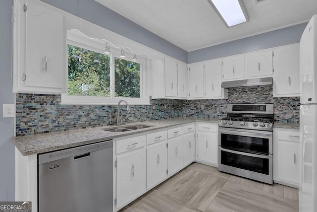 kitchen with white cabinets, backsplash, appliances with stainless steel finishes, light stone counters, and sink