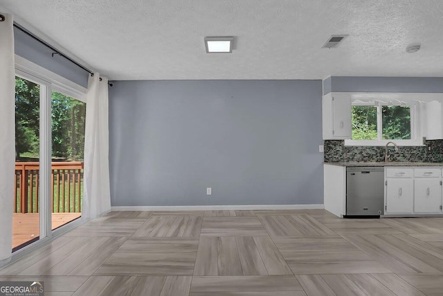 kitchen featuring white cabinetry, backsplash, stainless steel dishwasher, and a textured ceiling