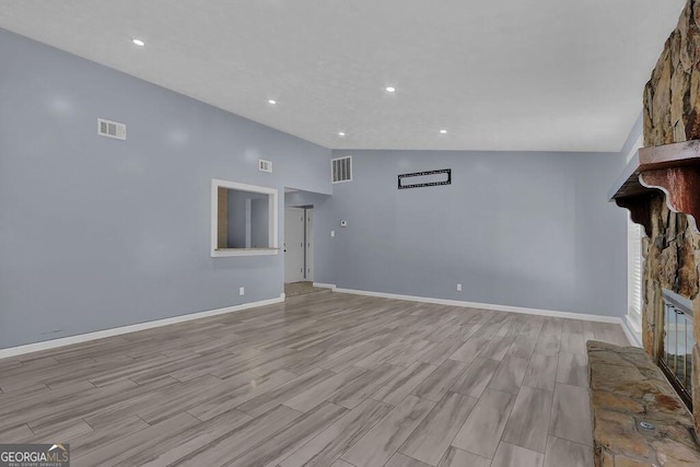 unfurnished living room with vaulted ceiling, a stone fireplace, and light hardwood / wood-style floors