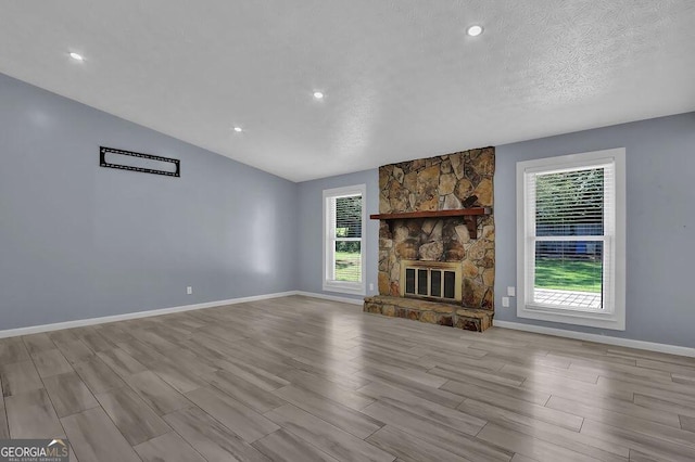 unfurnished living room featuring a stone fireplace, baseboards, a textured ceiling, lofted ceiling, and wood finished floors
