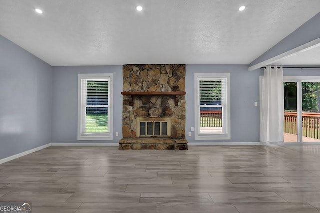 unfurnished living room with a textured ceiling, a healthy amount of sunlight, a stone fireplace, and light hardwood / wood-style flooring