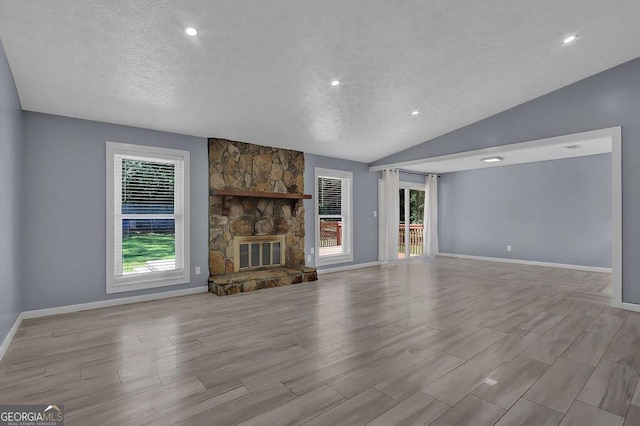 unfurnished living room with lofted ceiling, plenty of natural light, a textured ceiling, and a stone fireplace