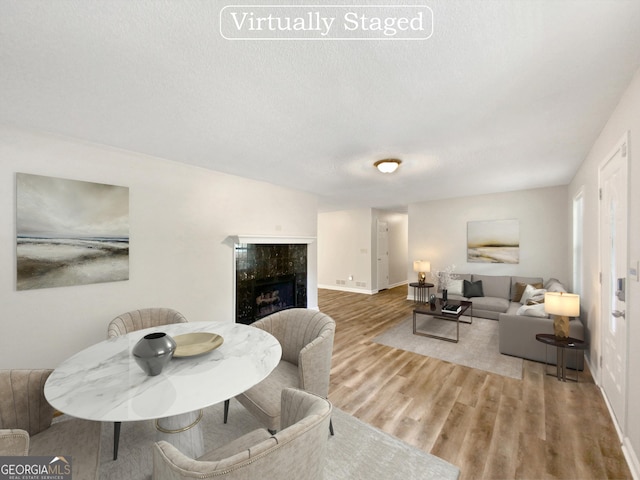 dining space featuring a high end fireplace, a textured ceiling, baseboards, and wood finished floors