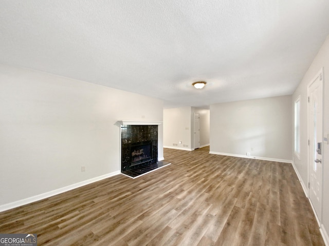 unfurnished living room featuring baseboards, a textured ceiling, wood finished floors, and a fireplace