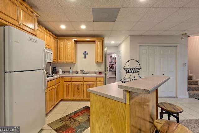 kitchen with a kitchen bar, white appliances, sink, and light tile patterned floors