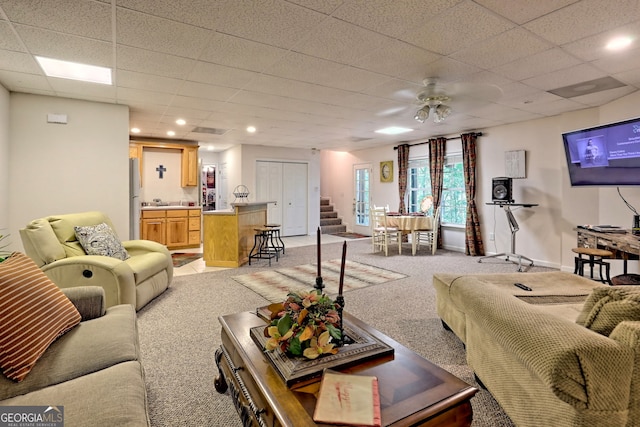 living room with a drop ceiling, light colored carpet, and ceiling fan