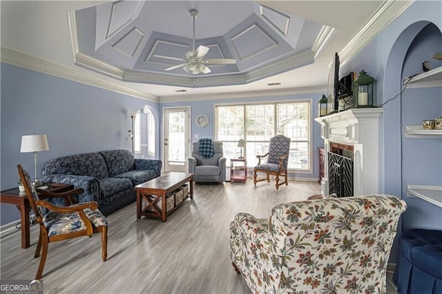 living room with ceiling fan, crown molding, a tray ceiling, and light hardwood / wood-style flooring