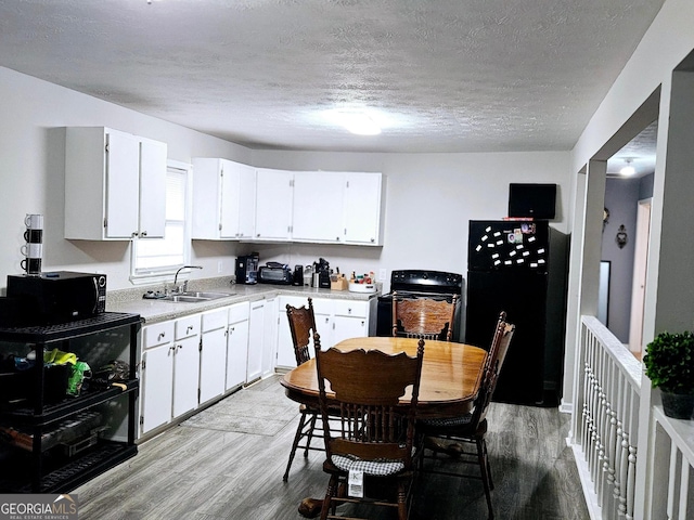 kitchen with light wood-type flooring, black appliances, white cabinetry, and sink