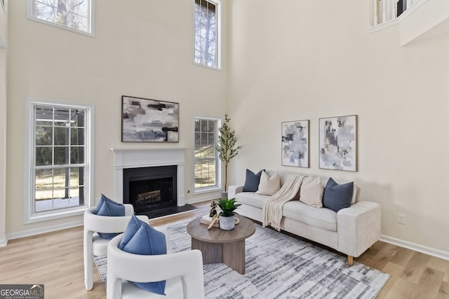 living area featuring a wealth of natural light, a fireplace, a towering ceiling, and wood finished floors