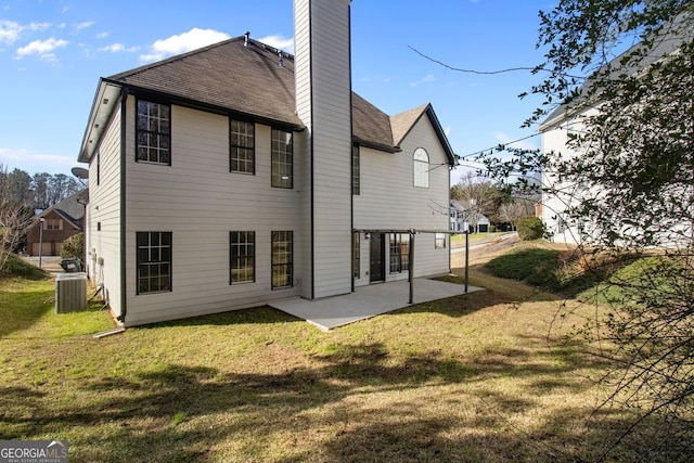 back of property featuring a chimney, central air condition unit, a shingled roof, a lawn, and a patio area