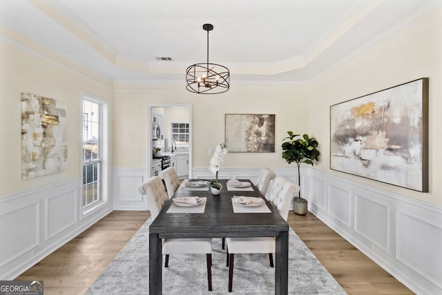 dining room featuring a tray ceiling, visible vents, a notable chandelier, and wood finished floors