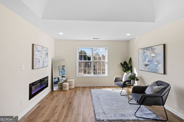 sitting room with light wood-type flooring, recessed lighting, baseboards, and a glass covered fireplace