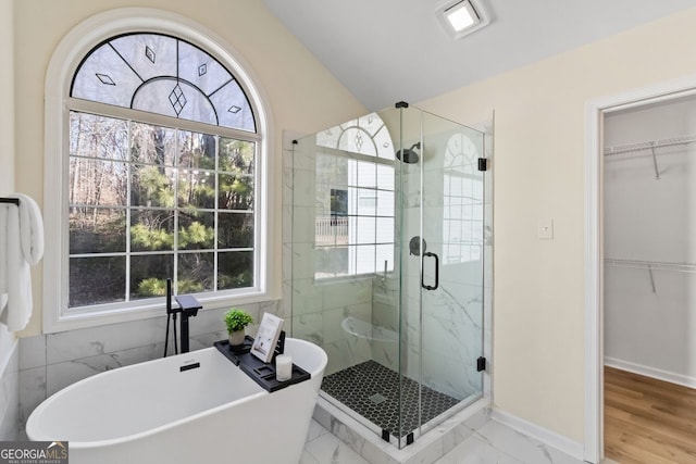 bathroom with marble finish floor, a freestanding bath, a spacious closet, a shower stall, and baseboards