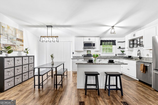 kitchen featuring a center island, appliances with stainless steel finishes, light stone countertops, white cabinetry, and dark wood-type flooring