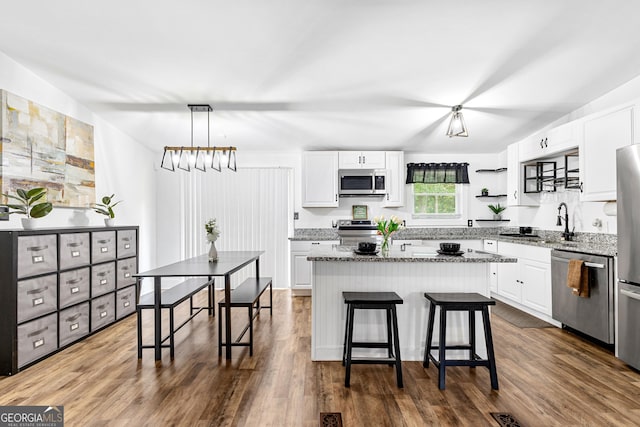 kitchen featuring light stone counters, a kitchen island, dark wood finished floors, white cabinetry, and appliances with stainless steel finishes