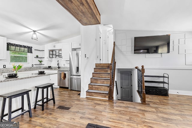 kitchen featuring white cabinets, light wood-type flooring, light stone counters, stainless steel appliances, and lofted ceiling