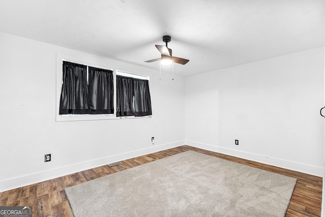 empty room with a ceiling fan, visible vents, wood finished floors, and baseboards