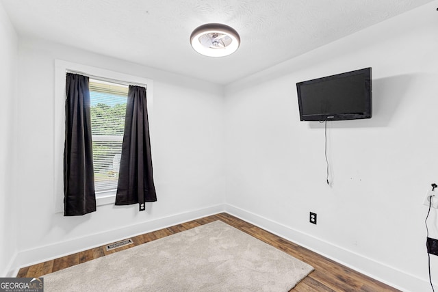 unfurnished room featuring visible vents, a textured ceiling, baseboards, and wood finished floors