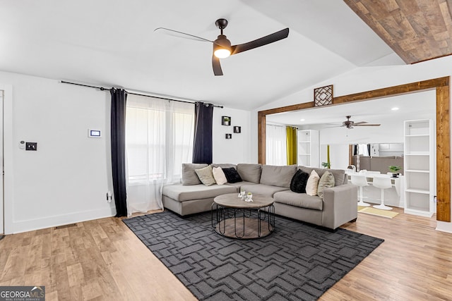 living area with light wood-type flooring, visible vents, baseboards, ceiling fan, and vaulted ceiling