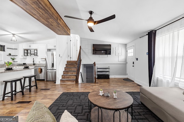 living area with ceiling fan, baseboards, stairway, lofted ceiling with beams, and wood finished floors