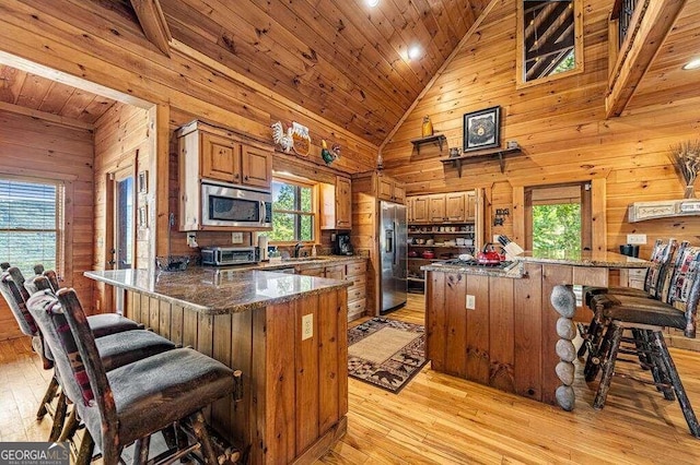 kitchen featuring sink, stainless steel appliances, light wood-type flooring, and wood walls