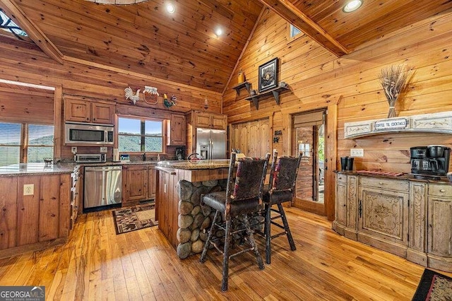 kitchen with a kitchen island, high vaulted ceiling, light hardwood / wood-style flooring, wood walls, and stainless steel appliances