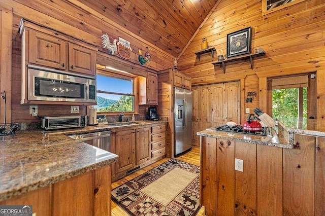 kitchen with appliances with stainless steel finishes, sink, light wood-type flooring, wooden walls, and high vaulted ceiling