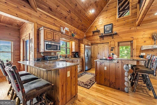 kitchen featuring wooden walls, sink, light wood-type flooring, appliances with stainless steel finishes, and high vaulted ceiling