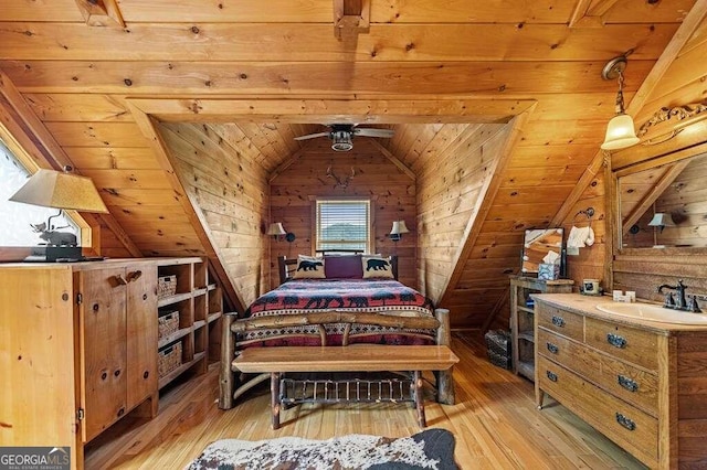 bedroom with light hardwood / wood-style flooring, lofted ceiling, sink, and wooden walls