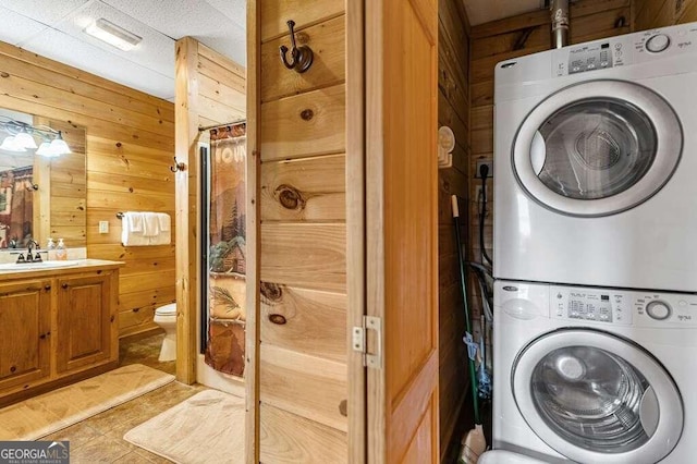 laundry area featuring wood walls, stacked washer and dryer, and sink