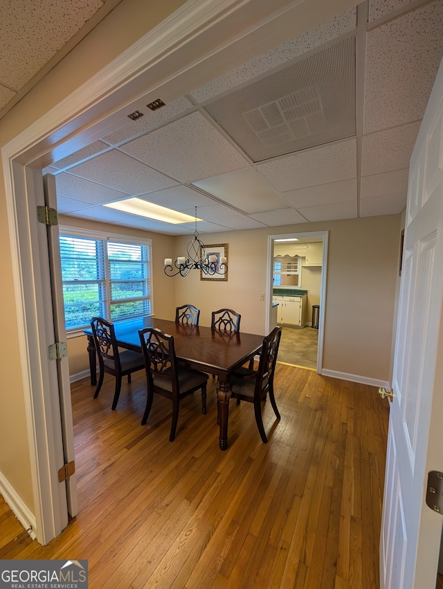 dining area with a paneled ceiling, light hardwood / wood-style floors, and a notable chandelier