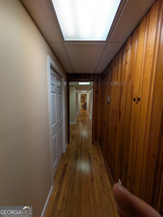 hall featuring hardwood / wood-style flooring, wooden walls, and a drop ceiling