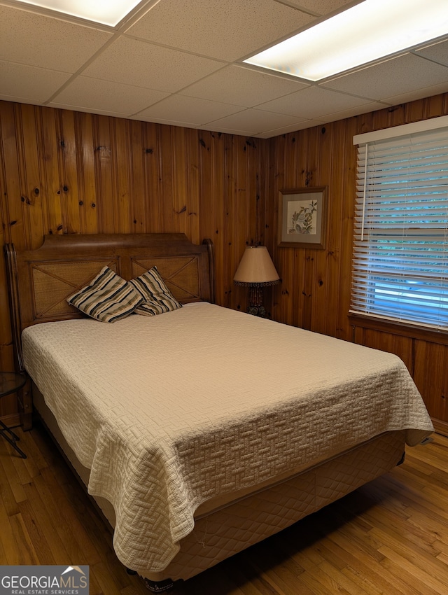 bedroom featuring hardwood / wood-style floors, a paneled ceiling, and wooden walls