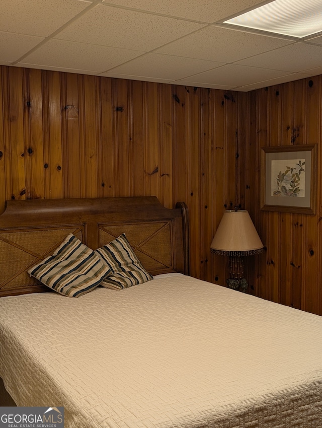 bedroom featuring a paneled ceiling and wooden walls