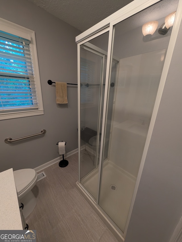 bathroom with hardwood / wood-style floors, toilet, an enclosed shower, and a textured ceiling